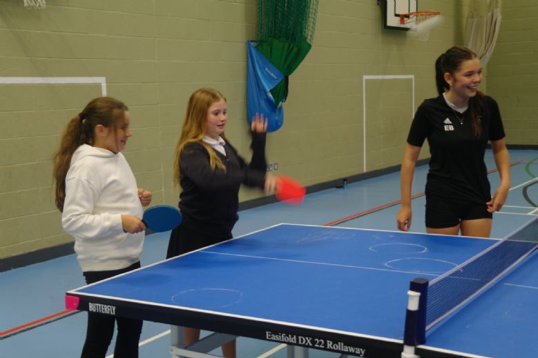 Pupils playing table tennis, guided by a Tibshelf Community School student volunteer.